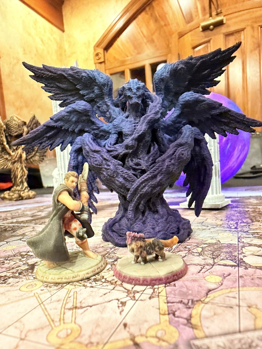 A tiny cat miniature facing down a giant winged monster on a game map