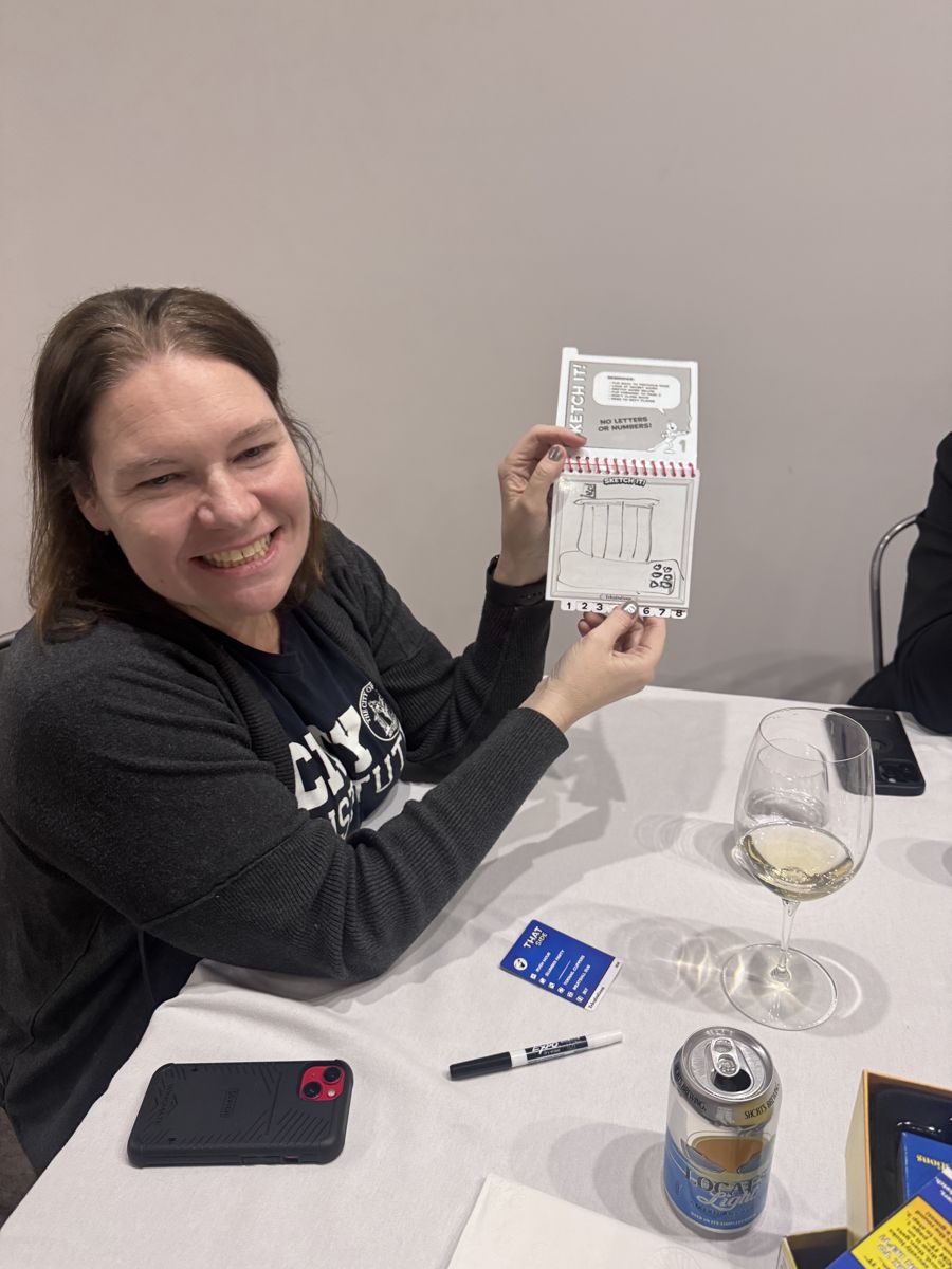 A woman laughing while showing her drawing during a game of Telestrations