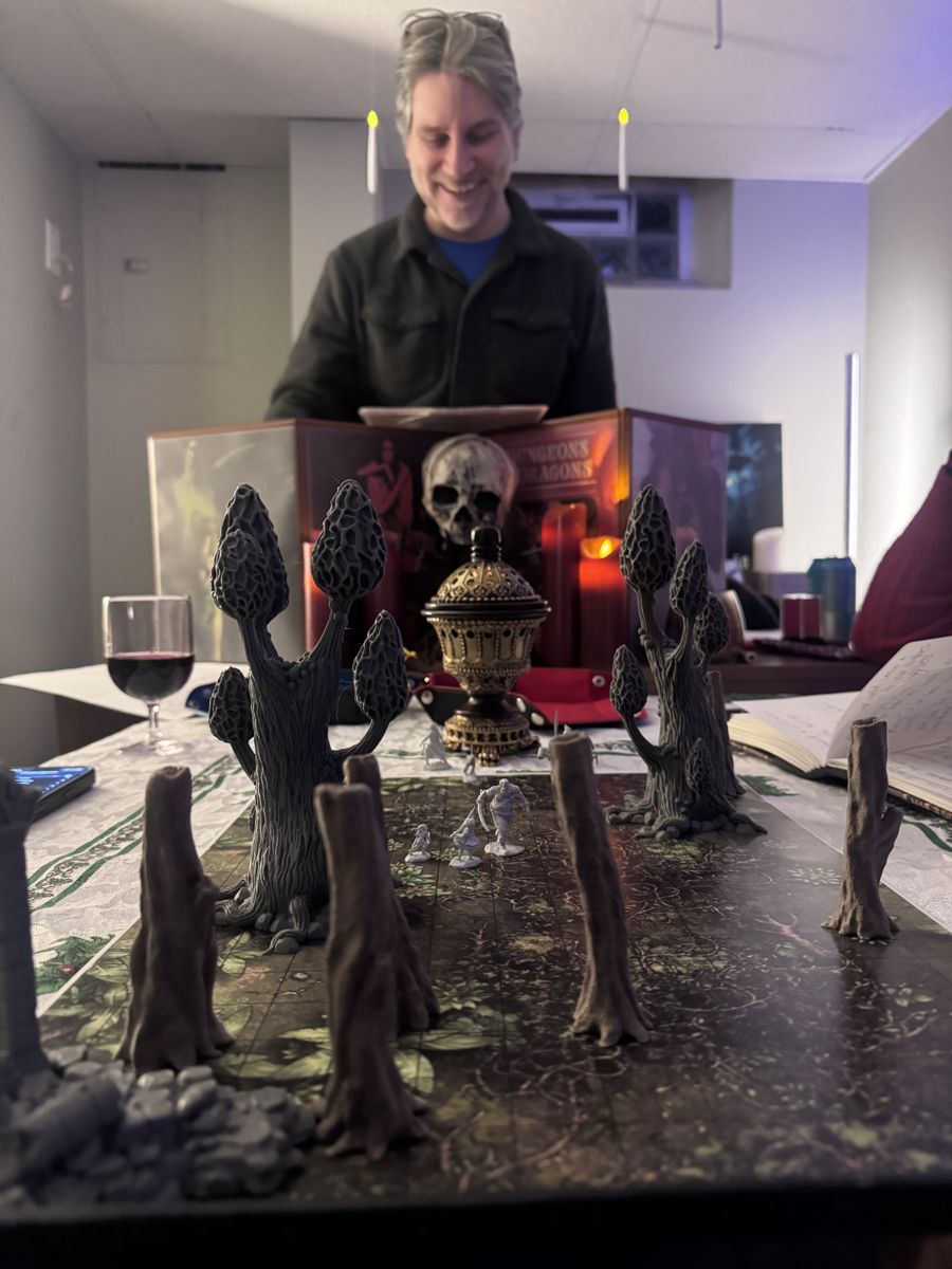 A smiling game master behind a Dungeons and Dragons screen with tiny mushroom terrain